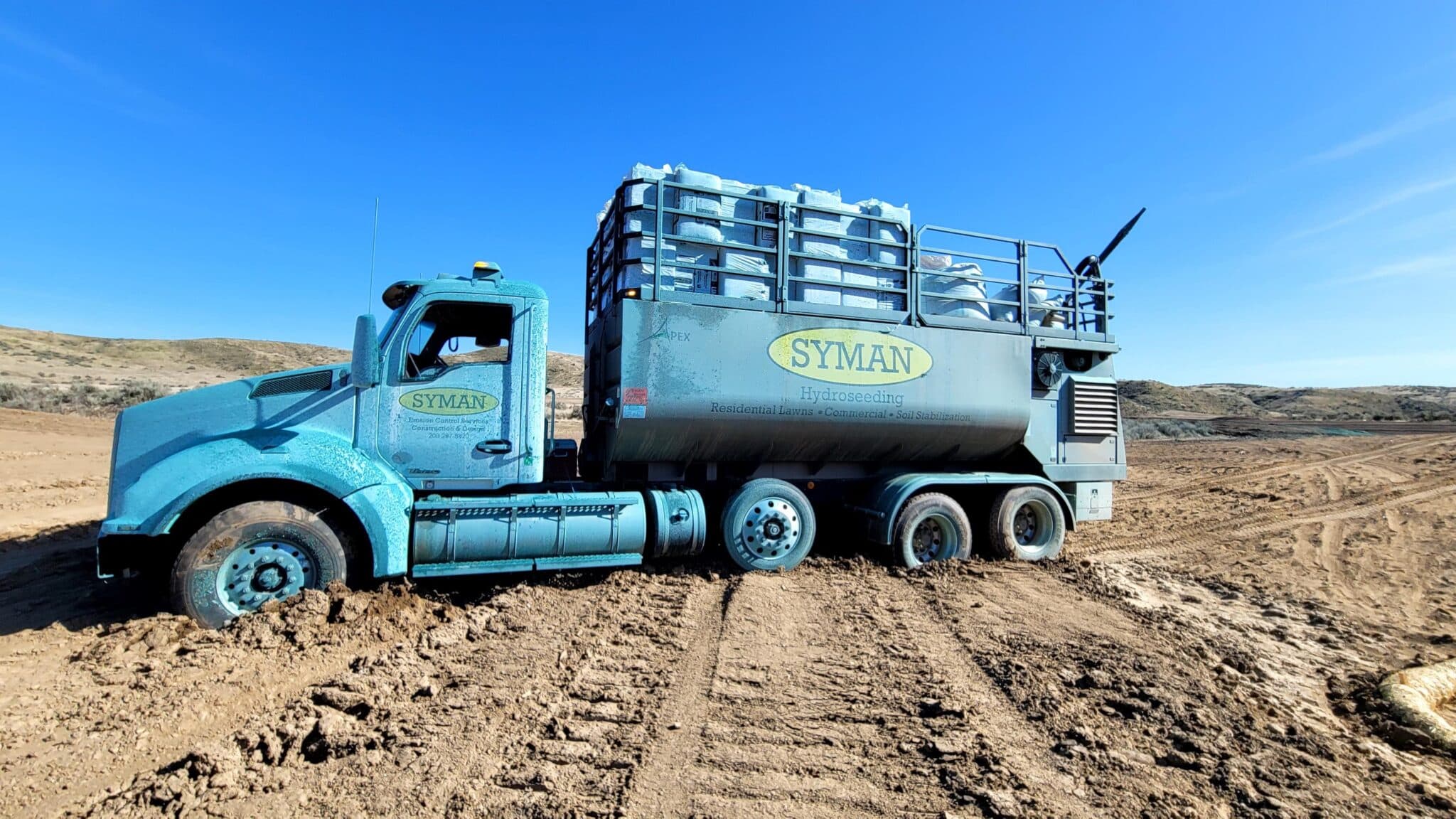 A close up of a blue Syman Inc truck in a dirt landscape with a backdrop of blue sky
